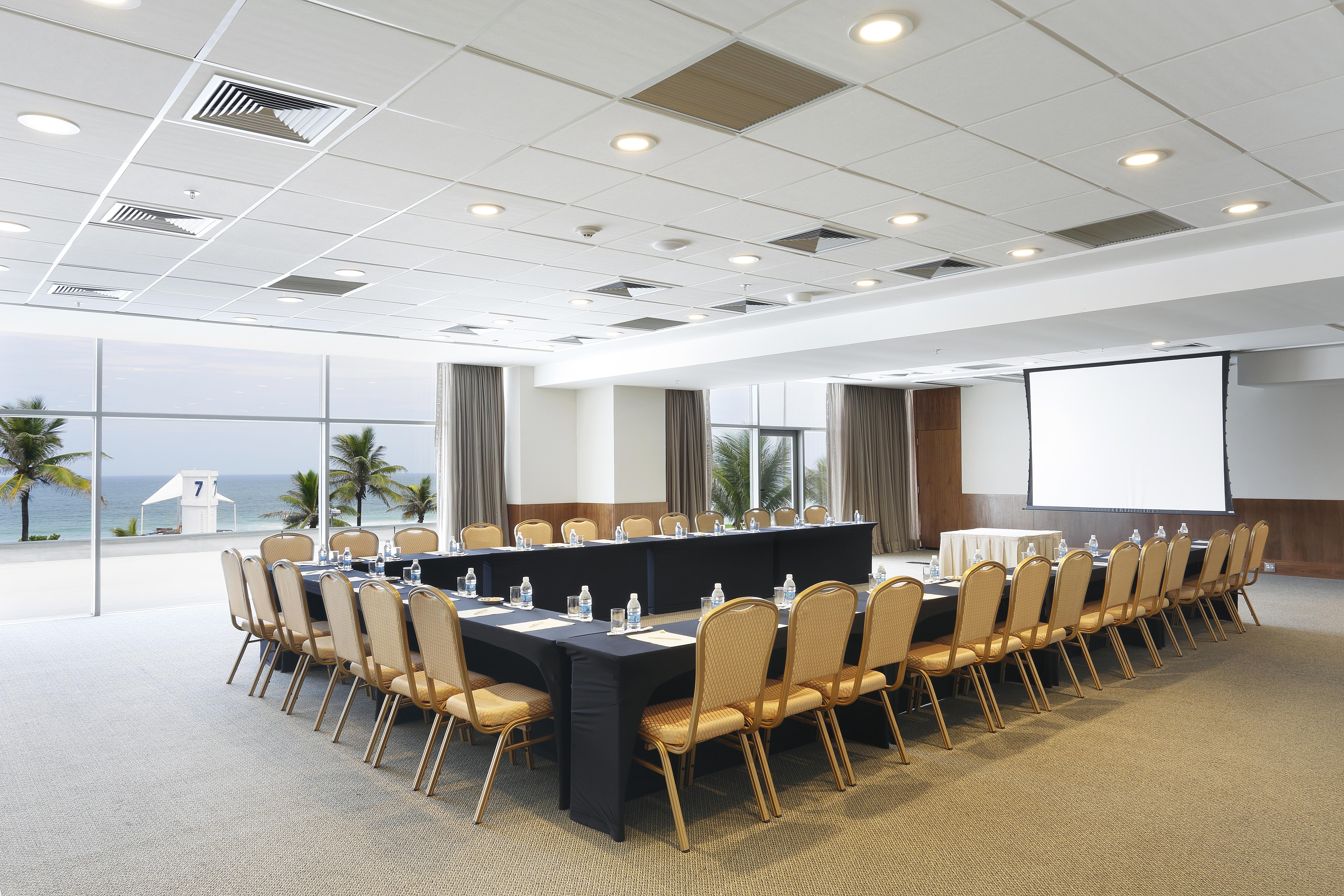 Windsor Marapendi Hotel Rio de Janeiro Ngoại thất bức ảnh The photo shows a spacious conference room set up for a meeting. It features a long, rectangular table surrounded by a number of beige chairs. At the front, there is a large screen, likely for presentations. The room has large windows that provide a 
