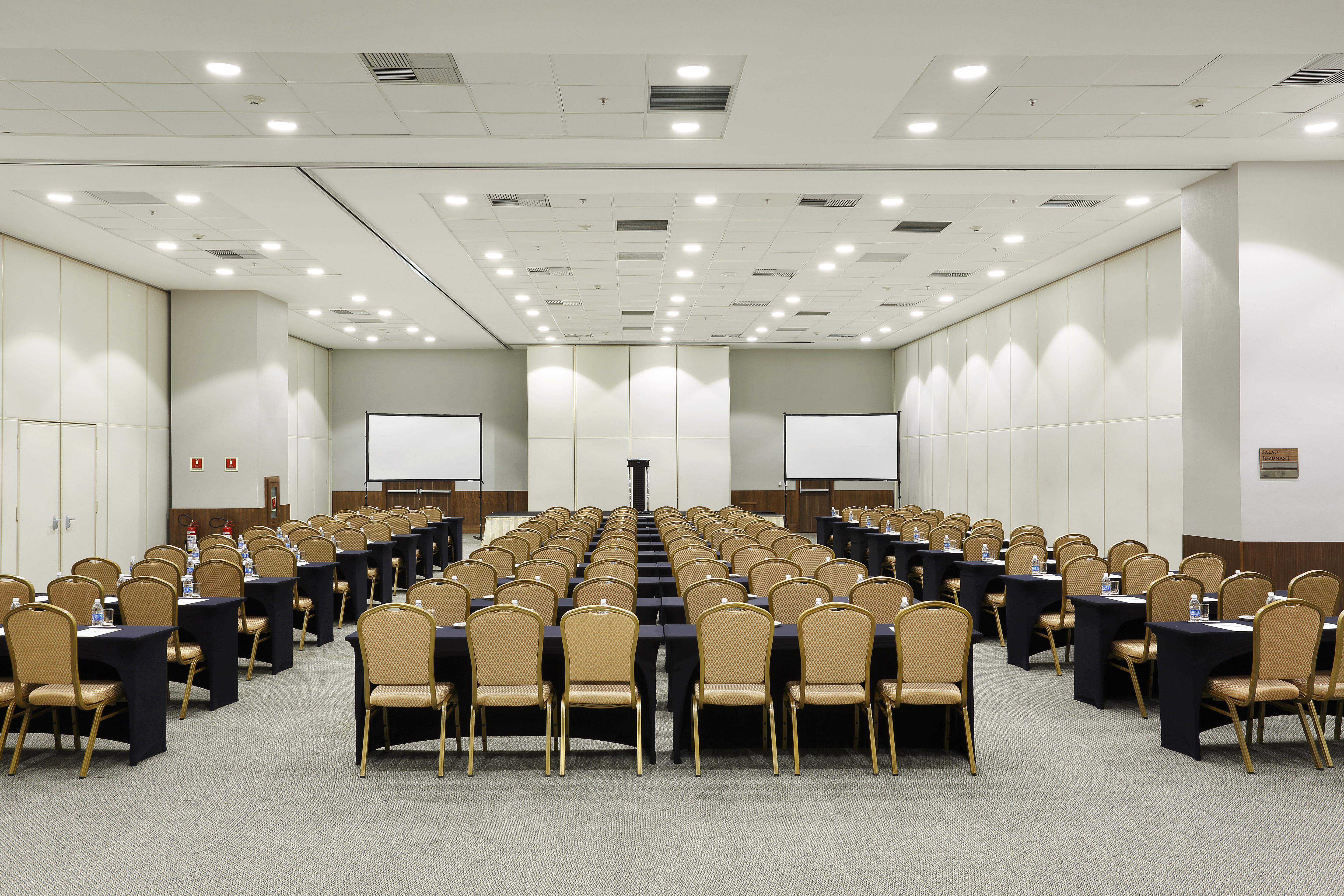 Windsor Marapendi Hotel Rio de Janeiro Ngoại thất bức ảnh The photo shows a conference room arranged for an event or meeting. There are rows of neatly arranged chairs with golden frames, paired with black tables. The room has bright overhead lighting and features two blank screens in the front, likely for p