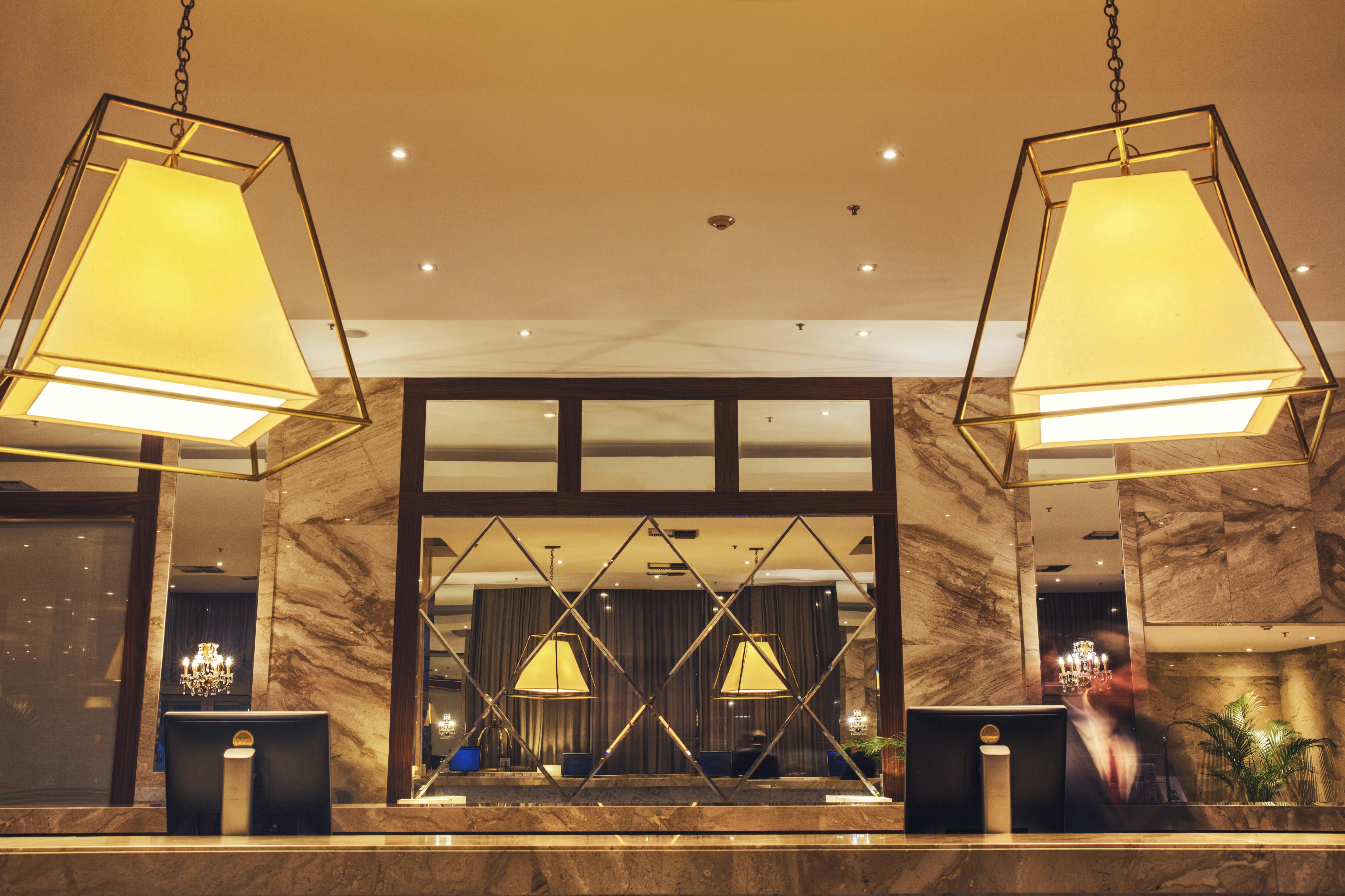 Windsor Marapendi Hotel Rio de Janeiro Ngoại thất bức ảnh The photo shows a hotel lobby or reception area. There are large geometric light fixtures hanging from the ceiling, providing a warm glow to the space. The reception desk is made of a polished material, likely marble, with decorative elements and two